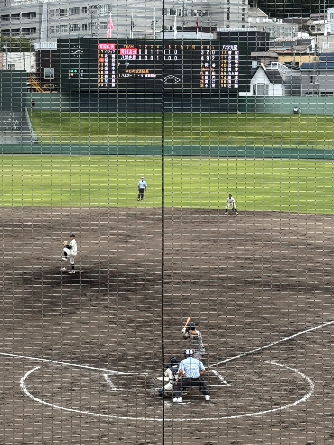 Aomori Yamada and Hachinohe Gakuin Kosei playing baseball, viewed through the backstop net